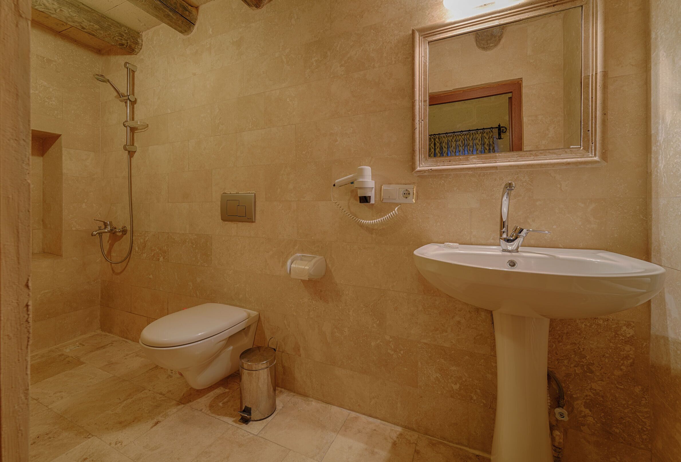 A bathroom with a toilet, sink, shower, and a trash can.