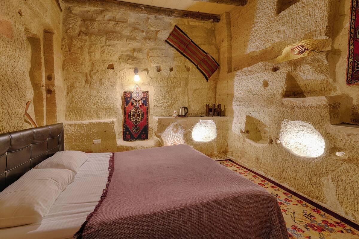 Una habitación de paredes de piedra con una cama, una lámpara colgante y una alfombra decorativa.