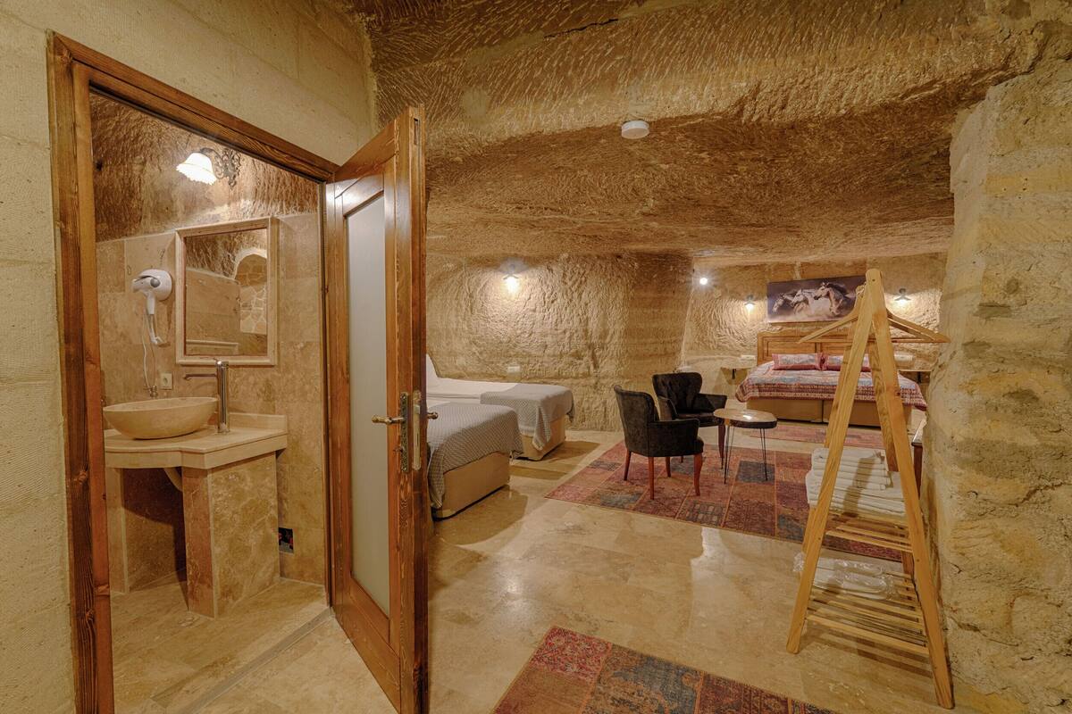 Una habitación con techo de piedra, una escalera de madera, una cama, una silla y un lavabo.