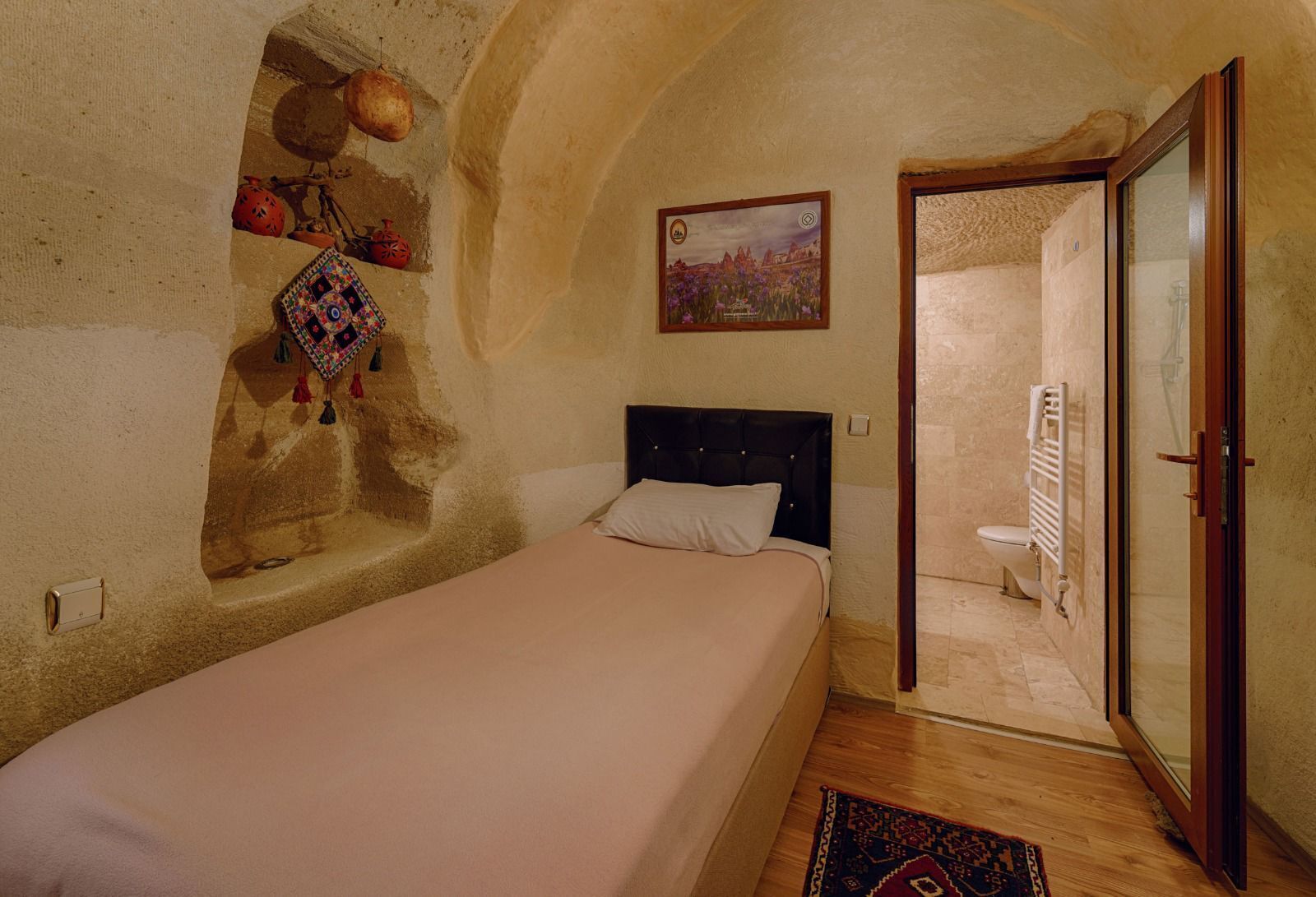 Un dormitorio con cama, un pequeño rincón decorado con objetos, un cuadro y vista al baño por una puerta abierta.