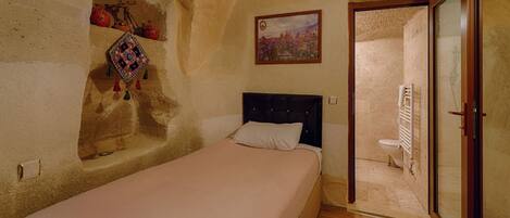 Un dormitorio con cama, un pequeño rincón decorado con objetos, un cuadro y vista al baño por una puerta abierta.