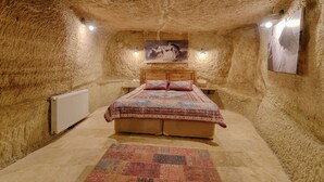 A cozy bedroom with a rustic stone wall, a wooden bed, and a patterned rug. - Avlu Cave House  (Nevsehir)