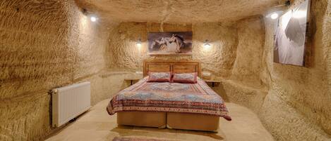 A cozy bedroom with a rustic stone wall, a wooden bed, and a patterned rug.