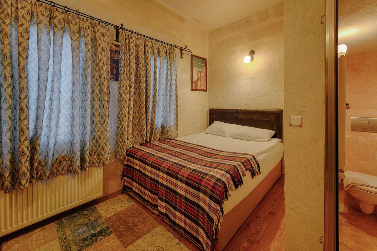 Un dormitorio con cama, cortinas, un radiador y un cuadro en la pared.