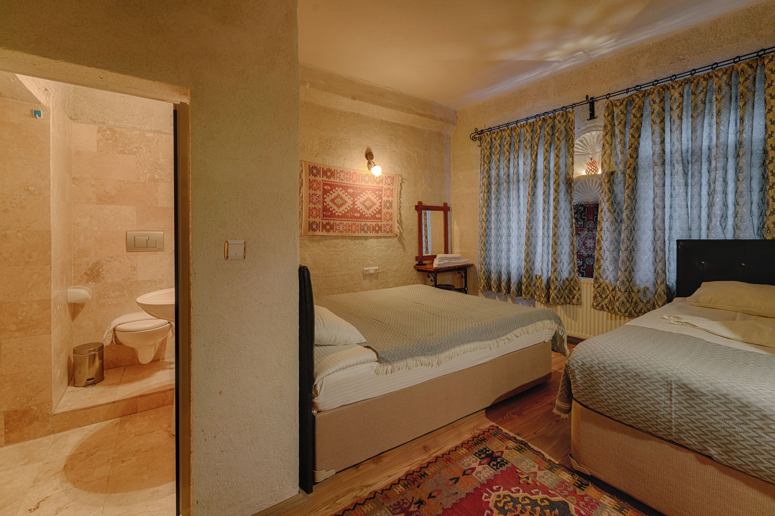 Un dormitorio con cama, mesita de noche, espejo y ventana con cortinas.