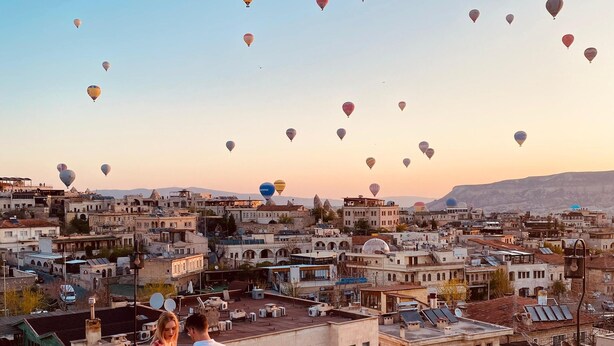 A rooftop terrace with a view of a cityscape and hot air balloons in the sky. - Avlu Cave House  (Nevsehir)