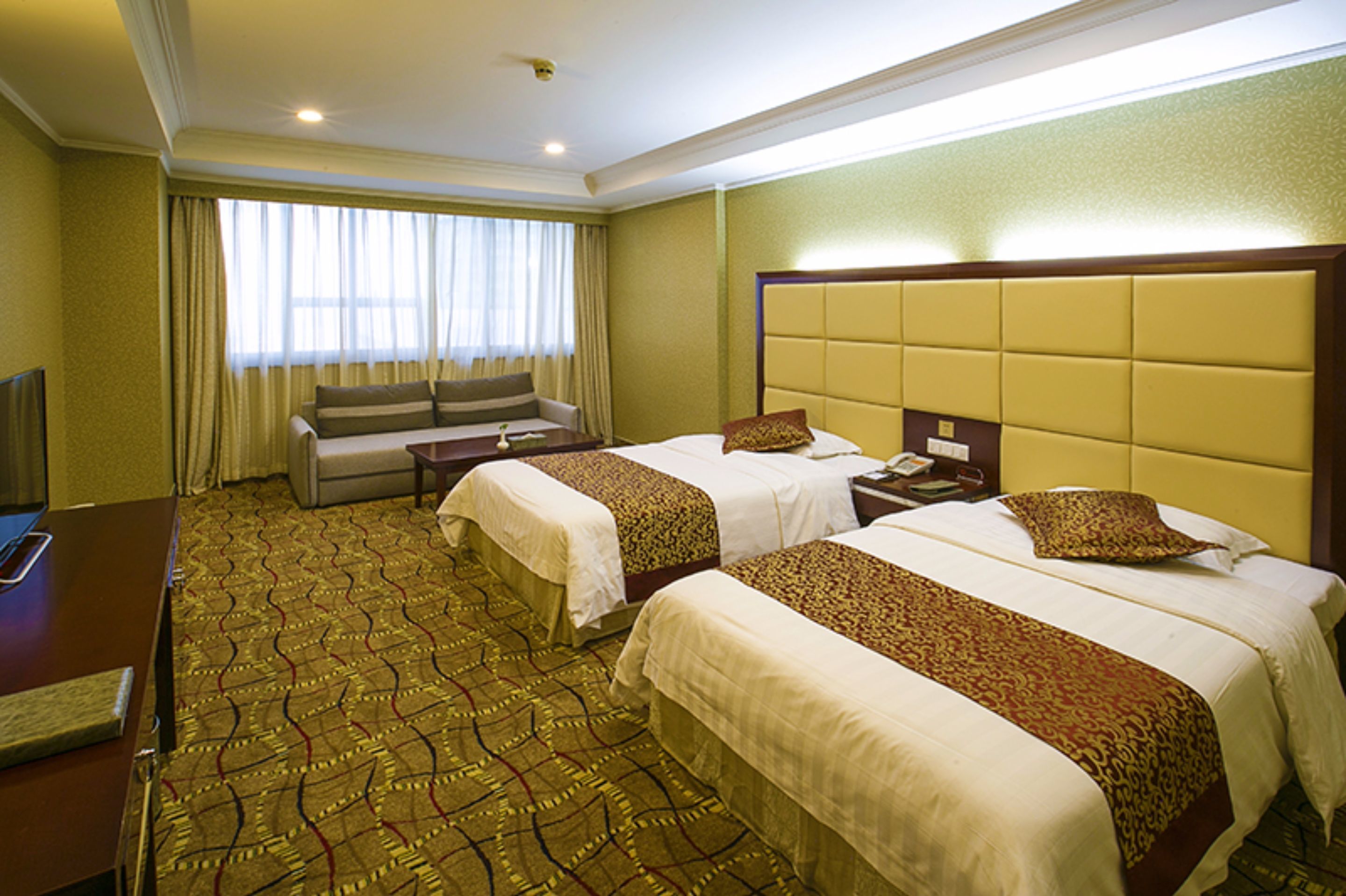 A hotel room with two beds, a sofa, a desk, and a television.