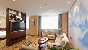 Ett hotellrum med en stor platt-TV, en soffa, ett soffbord och ett stort fönster med gardiner.