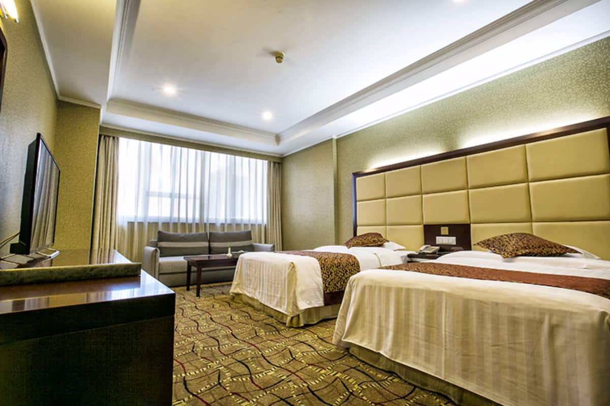 Quarto de hotel com duas camas, um sofá, uma escrivaninha e uma televisão.