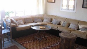 A living room with a beige sectional sofa, a round coffee table, a patterned rug, and a small wooden stool. - Odyssey Guest House (Bergama)