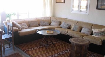 Una sala de estar con un sofá seccional color beige, una mesa de centro redonda, una alfombra estampada y un taburete de madera.