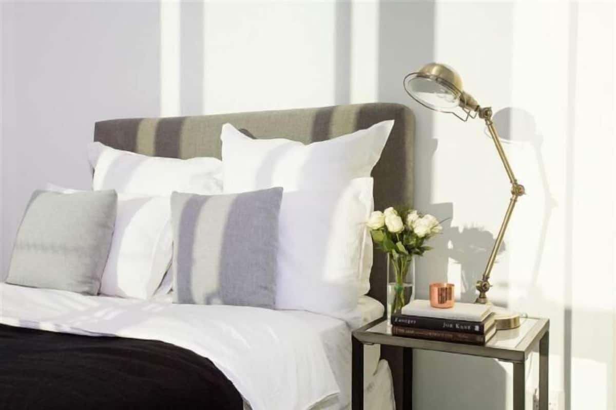 A neatly made bed with pillows, a bedside table with a lamp, a vase with flowers, and a book.