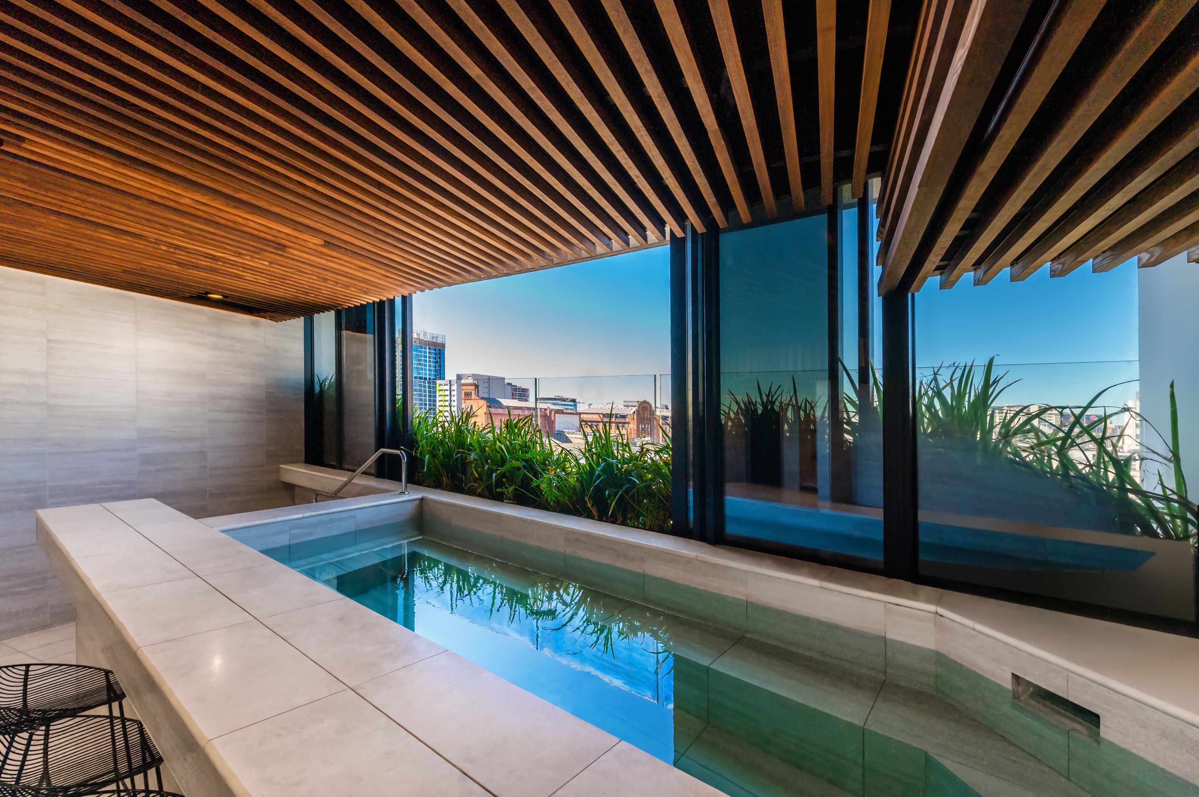 A modern indoor pool with a wooden ceiling, large windows, and a view of the cityscape.