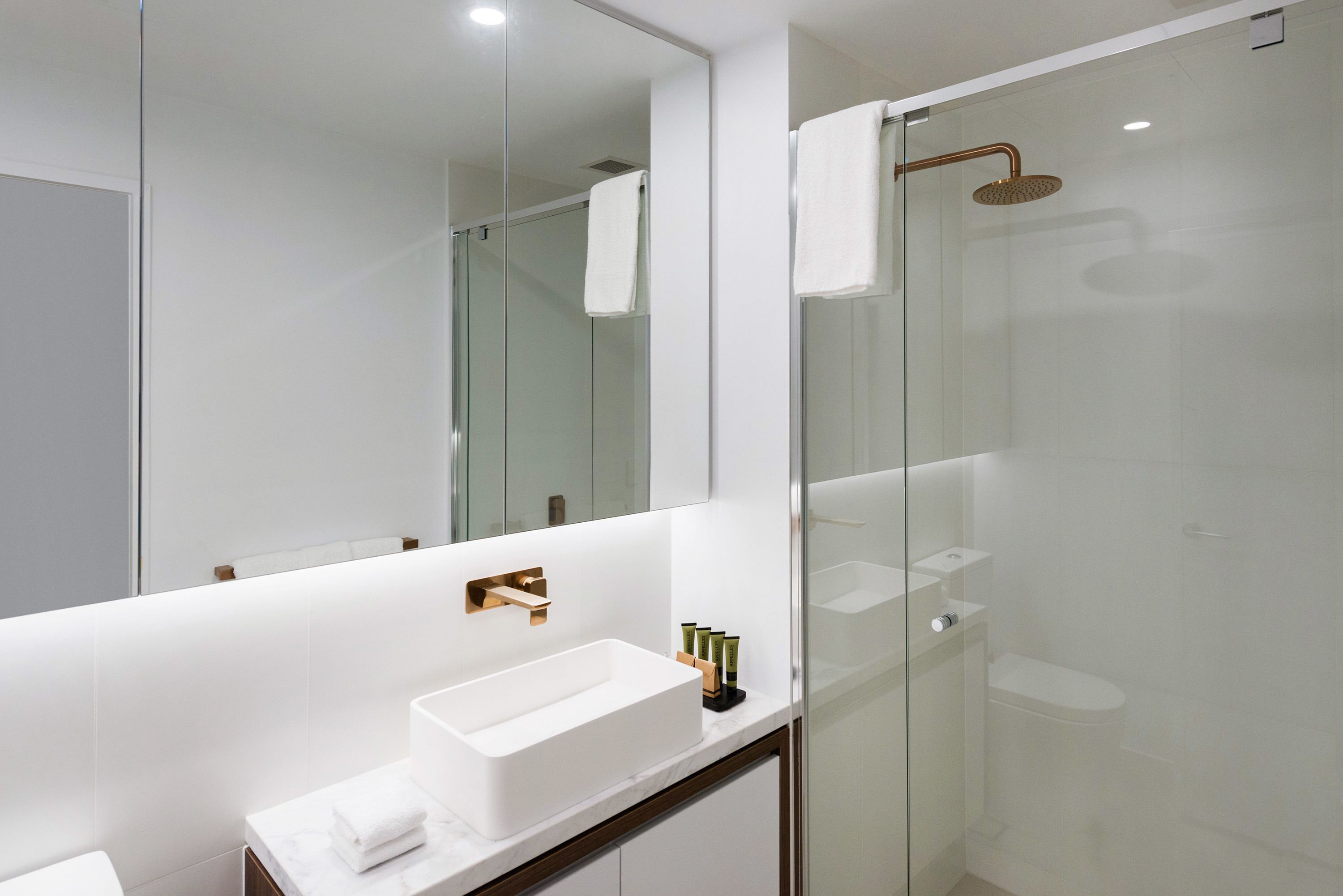 A modern bathroom with a white sink, a large mirror, and a glass-enclosed shower area.
