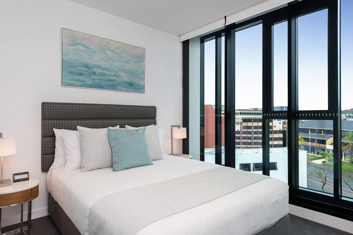 A hotel room with a large bed, a headboard, a nightstand, a lamp, and a painting on the wall.