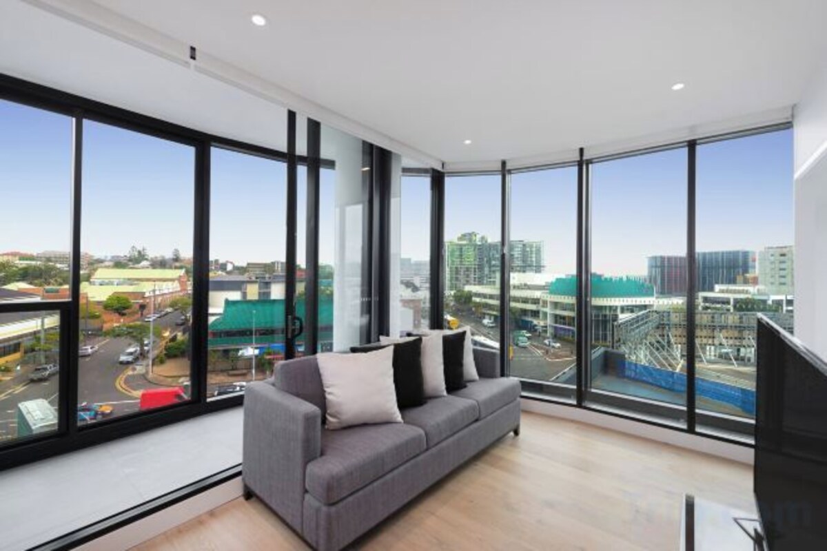A modern living room with a large window, a grey sofa, and a flat-screen TV.