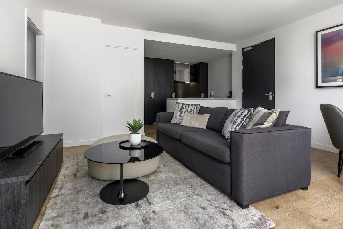 A modern living room with a grey sofa, a round coffee table, and a TV on a stand.