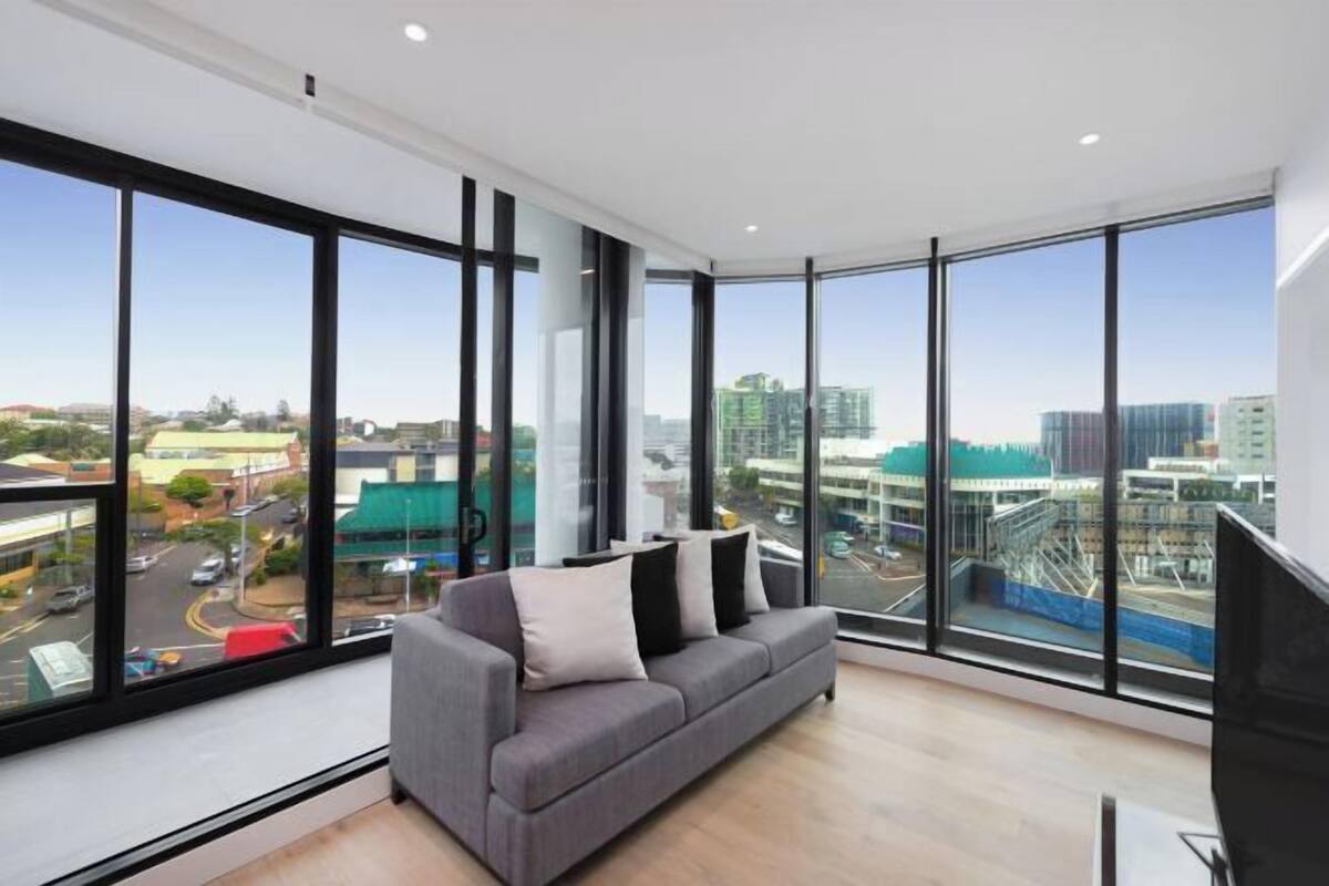 A modern room with large windows, a grey sofa, and a flat-screen TV.