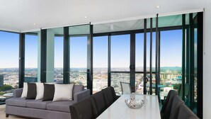 A modern living room with a sofa, dining table, and chairs, large windows with a city view.