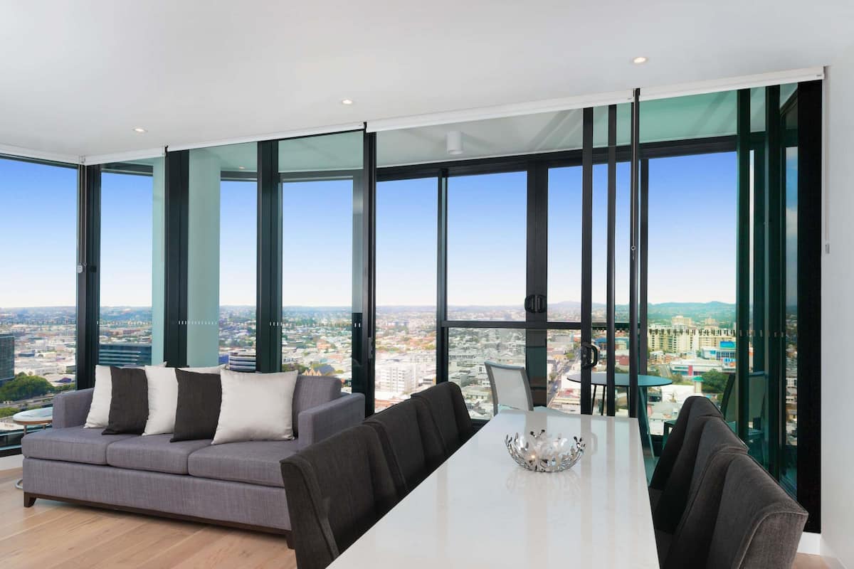 A modern living room with a sofa, dining table, and chairs, large windows with a city view.