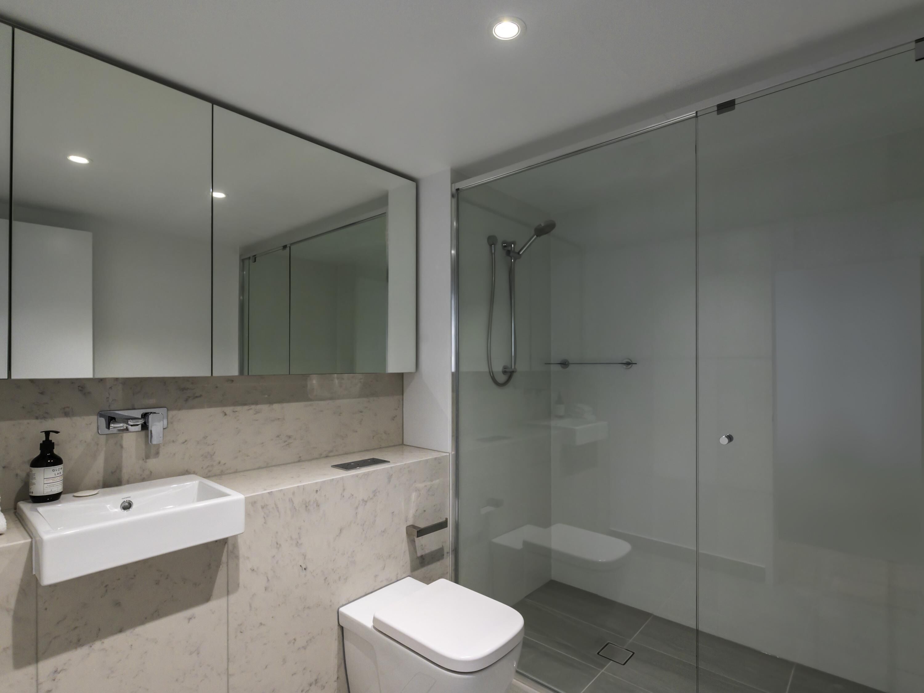 A modern bathroom with a glass shower enclosure, a white sink, and a toilet.