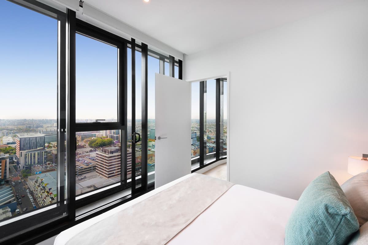 A modern bedroom with a large window, a bed, and a view of a cityscape.