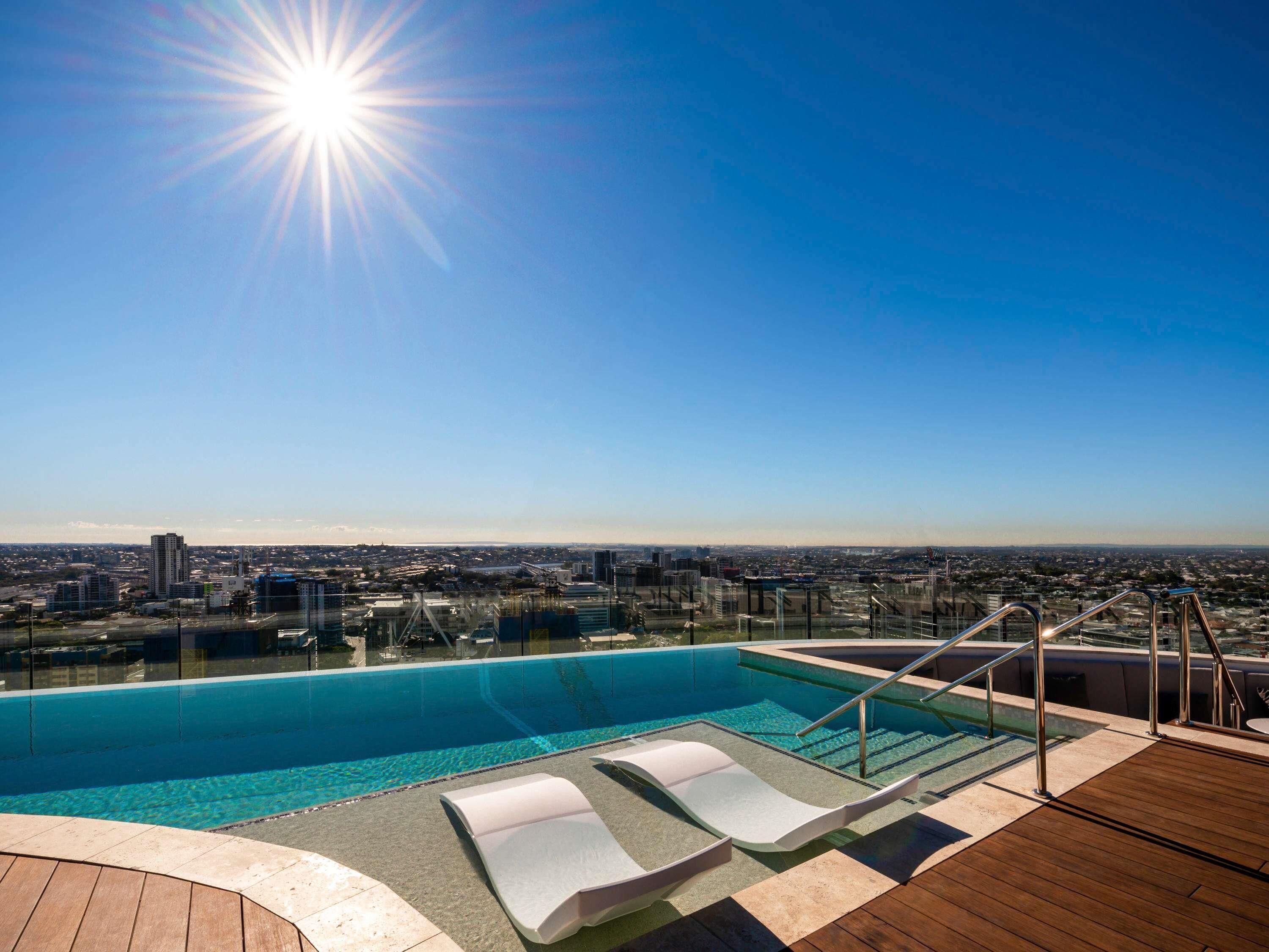 Ein Pool auf dem Dach mit Liegestühlen, freier Blick auf die Stadtlandschaft und ein sonniger Himmel.