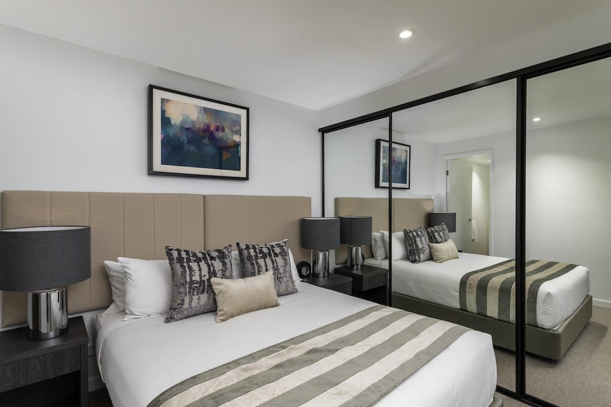 A hotel room with a large bed, two bedside tables with lamps, a mirror, and a painting on the wall.