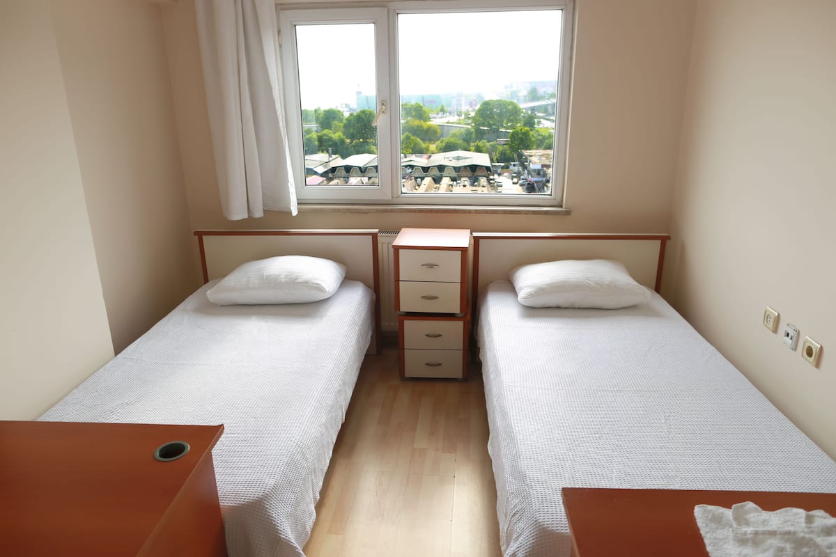 A twin room with two single beds, a small wooden dresser, and a window with a city view.