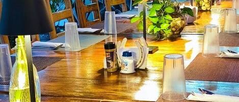 A restaurant interior with a wooden table set for dining, a chalkboard menu, and tropical decor.