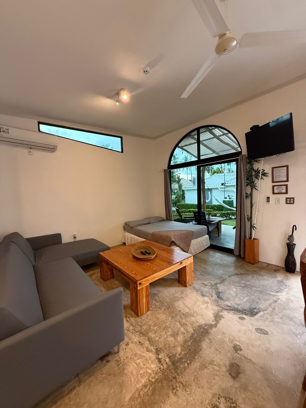 Una sala de estar moderna con un sofá gris, una mesa de centro de madera y un ventanal con vistas a zonas verdes.