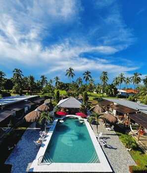 Un resort con piscina, palmeras y construcciones de techo de paja.