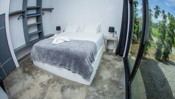 Ein modernes Schlafzimmer mit einem großen Bett, Einbauschränken, Nachttischen und Blick auf Palmen durch ein Fenster.