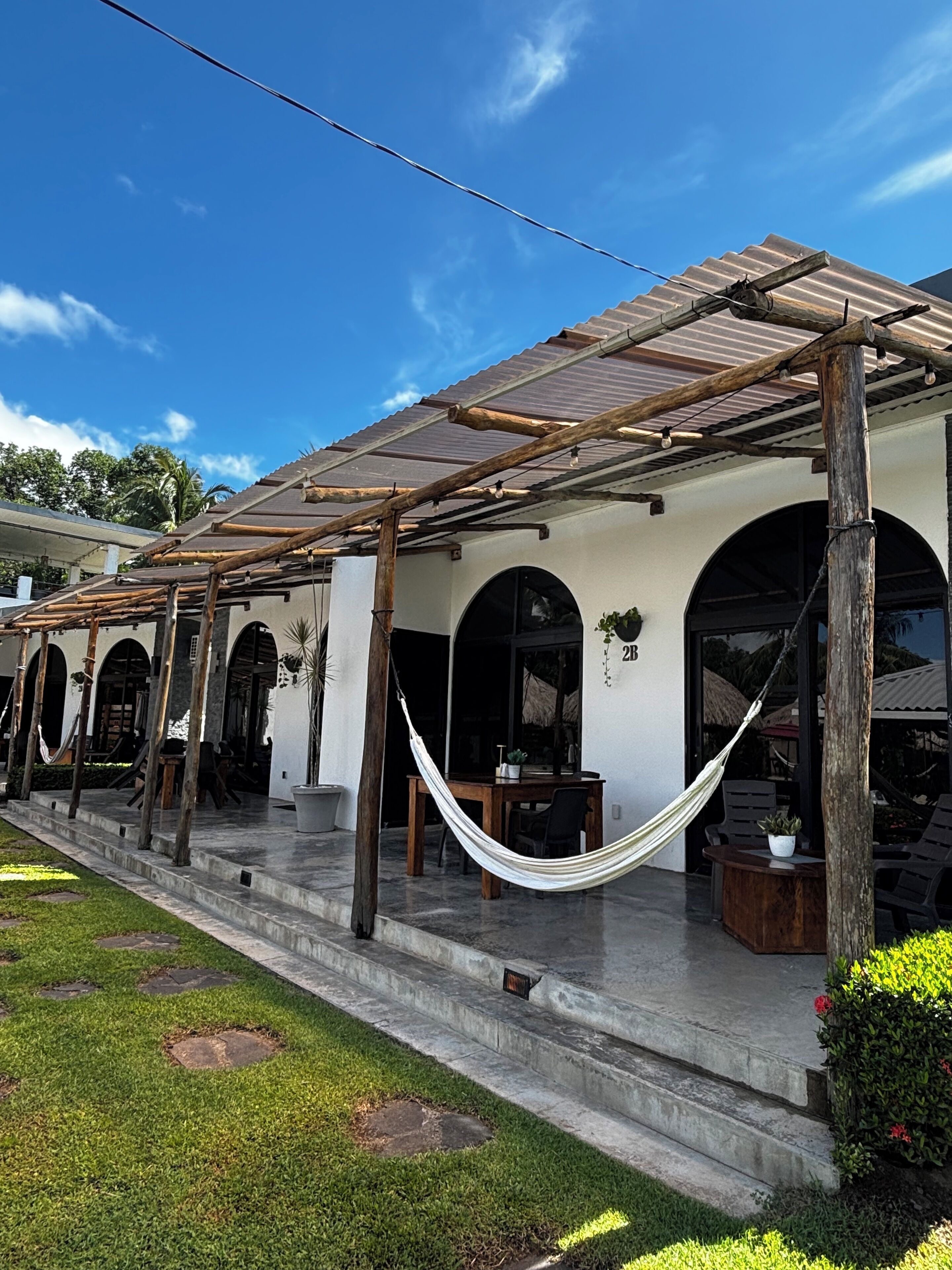 A covered outdoor area with a wooden pergola, a hammock, and a seating area with a table and chairs.