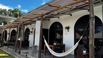 A covered outdoor area with a wooden pergola, a hammock, and a seating area with a table and chairs.