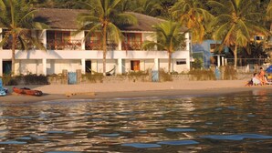 Una propiedad frente a la playa con un edificio de dos pisos, palmeras y una playa arenosa.