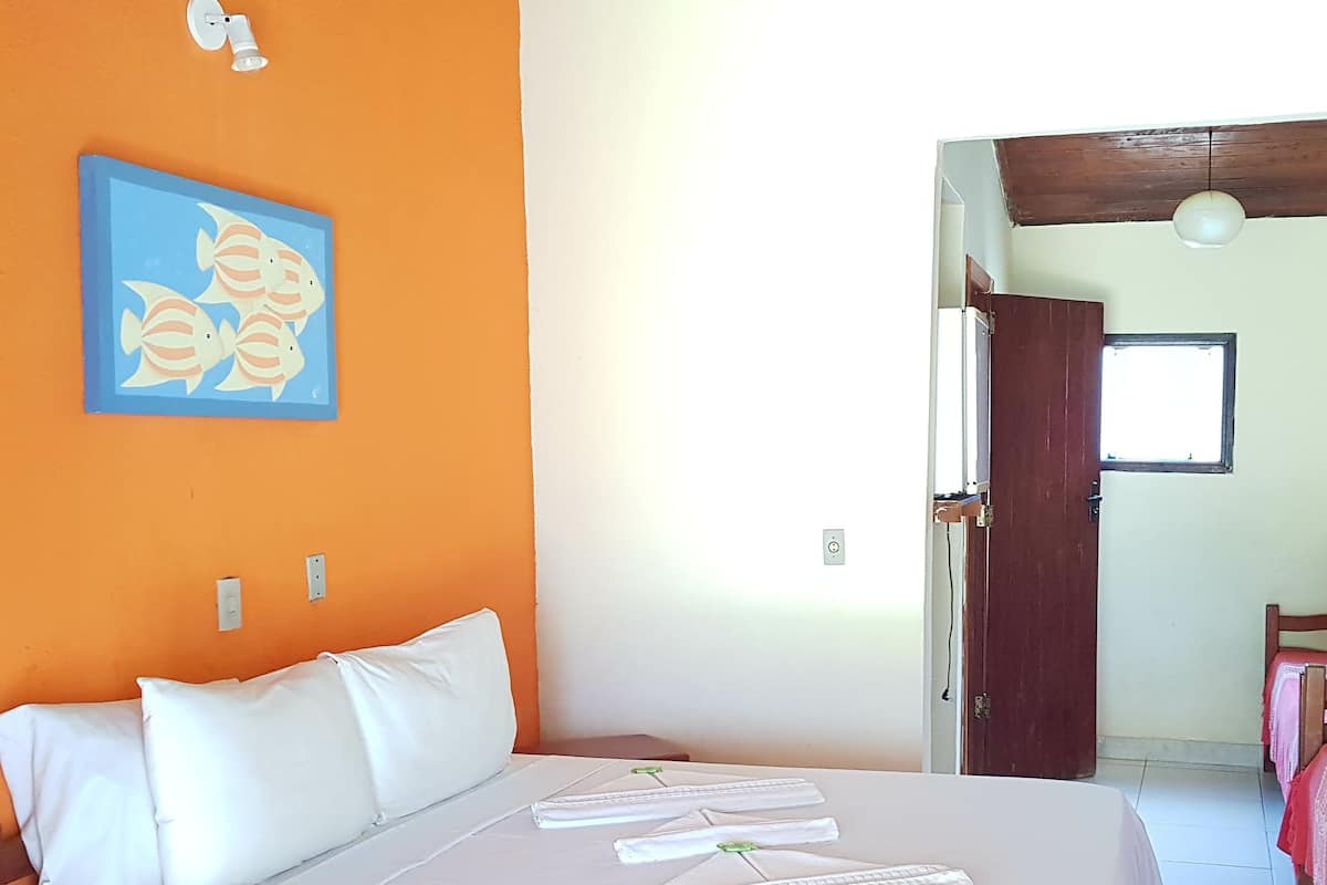 Quarto com cama, almofadas, uma parede com pintura, uma janela e uma porta.
