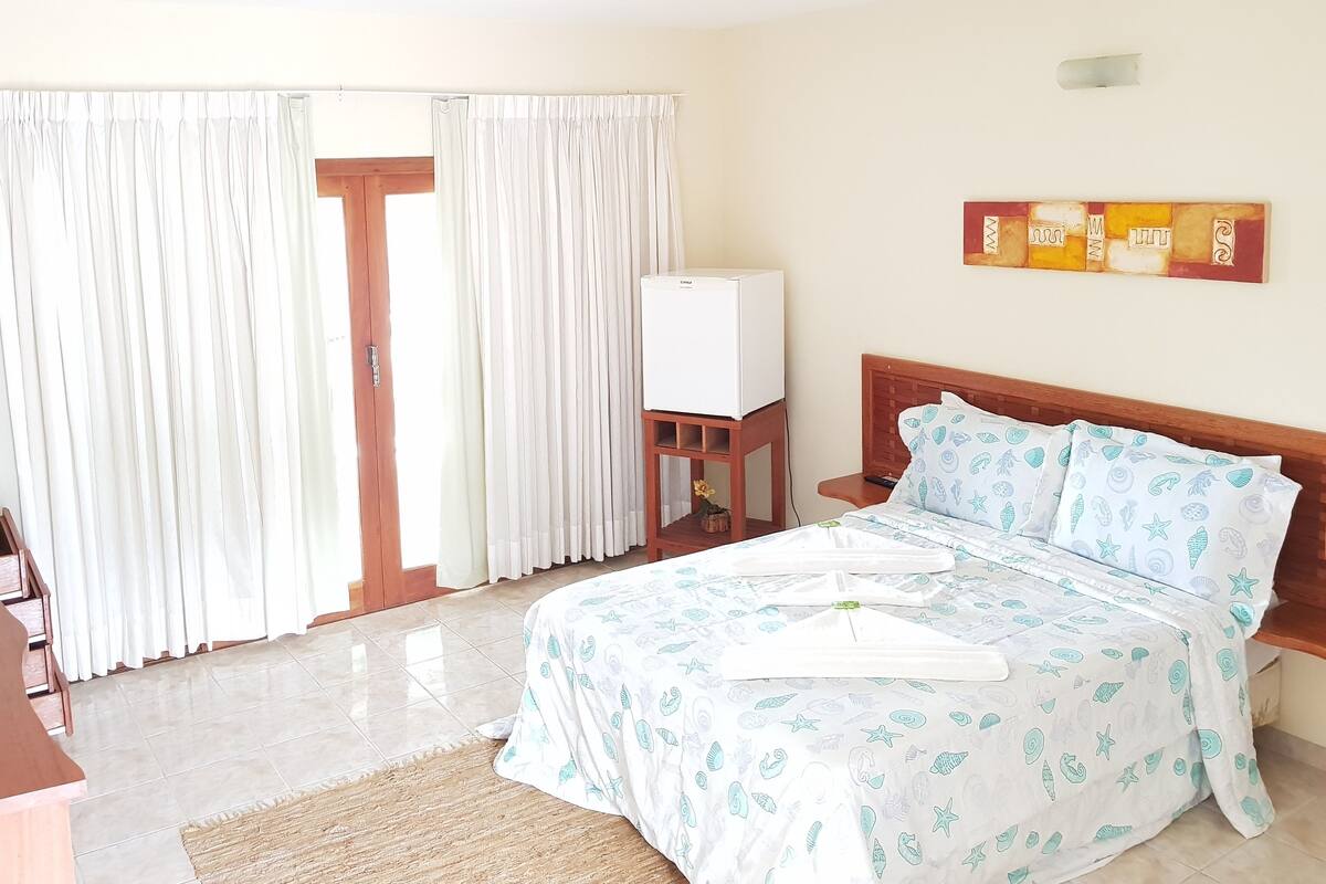 Quarto com cama, cortinas, televisão em móvel e quadro na parede.