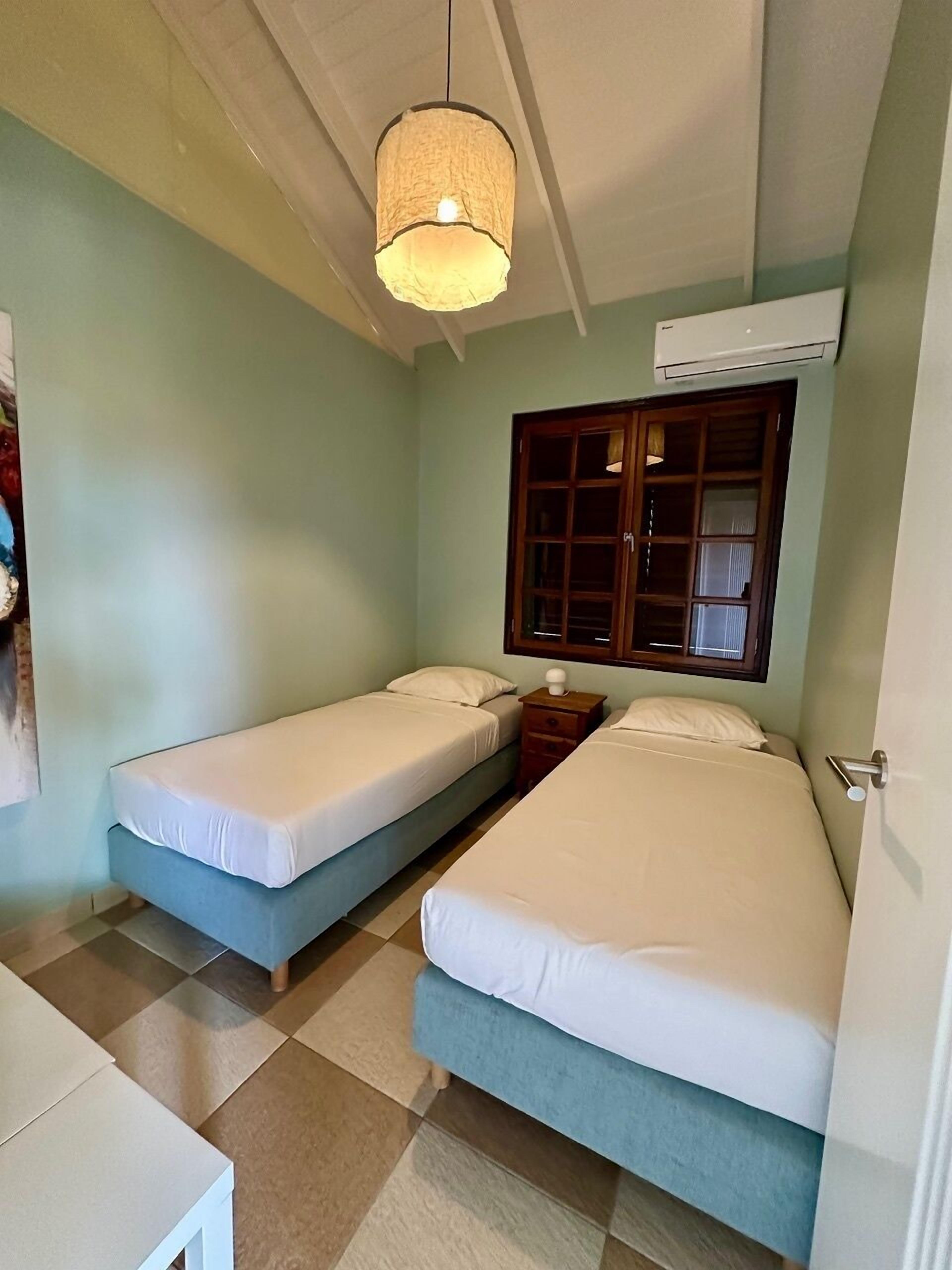 Une chambre avec deux lits simples, une armoire en bois, un luminaire suspendu et un appareil de climatisation.