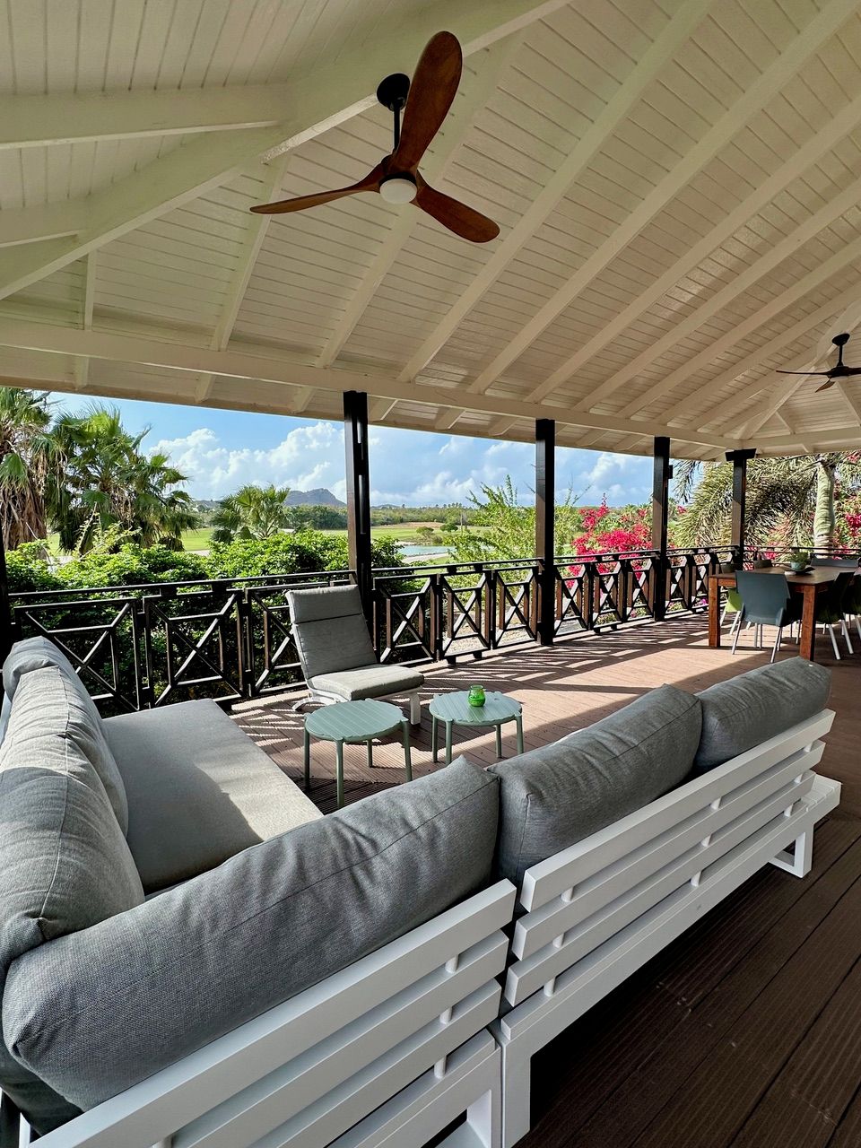 An outdoor patio with a white ceiling, ceiling fans, a sofa, and tables.