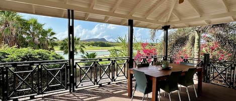 A covered outdoor area with a table and chairs, a wooden deck, and a view of a golf course and mountains.
