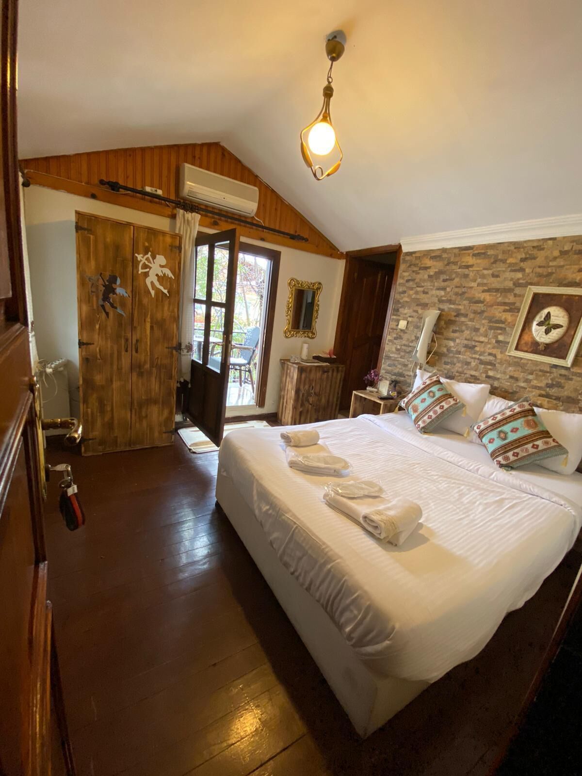 Un dormitorio con una cama grande, paredes de madera, una pared de acento de piedra, un espejo y una lámpara colgante.