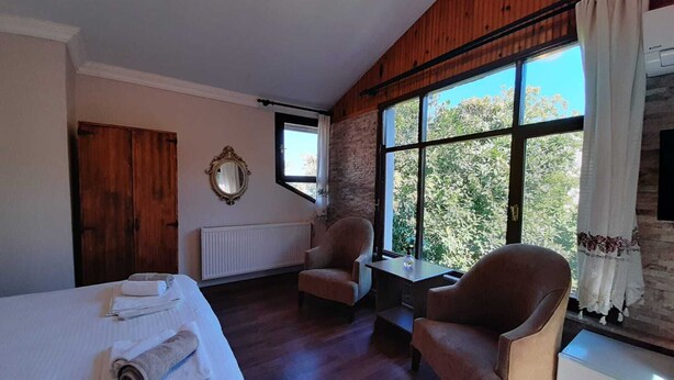 A hotel room with a bed, two armchairs, a small table, a radiator, a window with curtains, and a mirror on the wall. - Butik Hotel Masukiye (Kartepe)