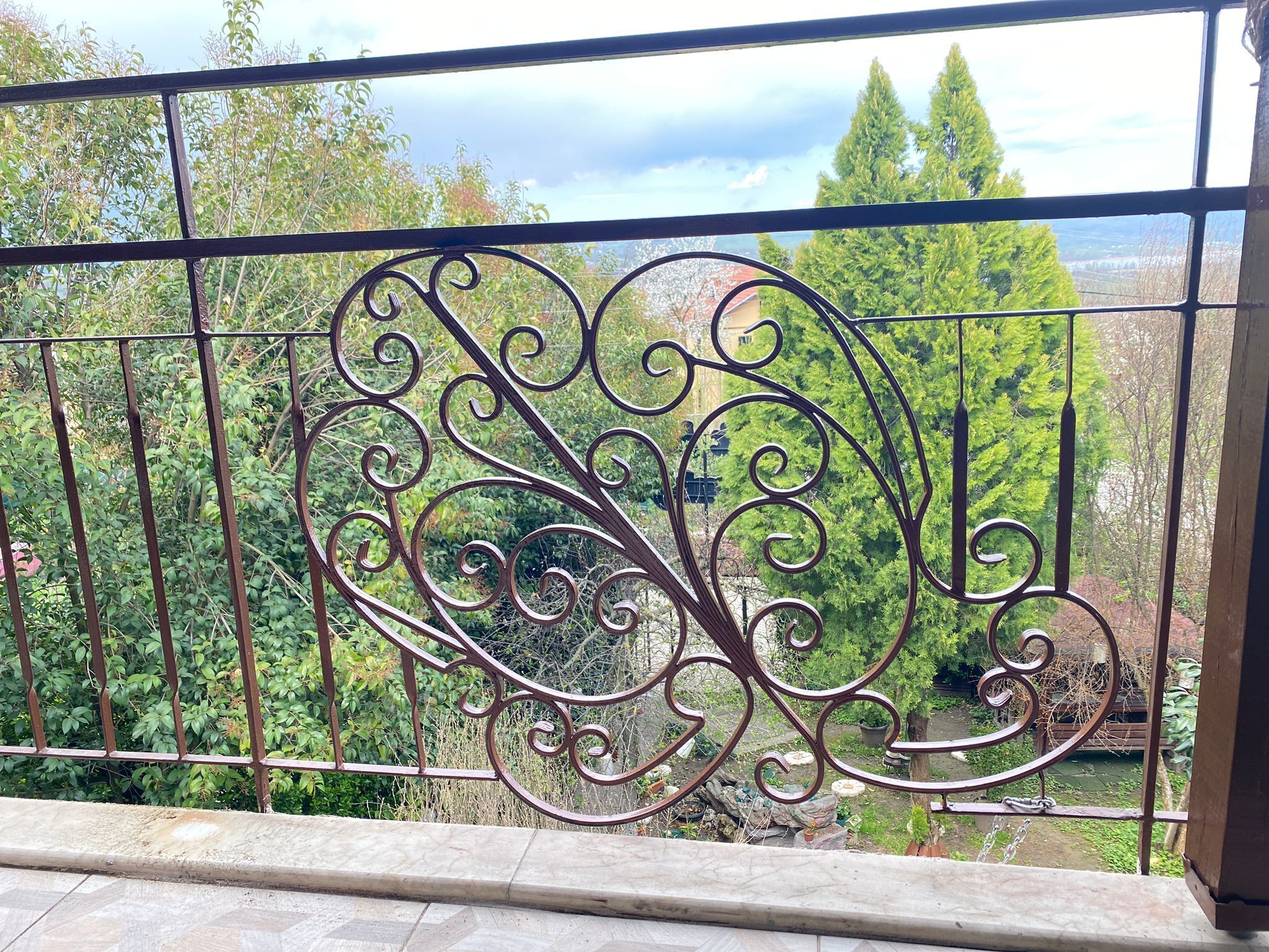 A balcony with ornate metal railings overlooking a garden and distant landscape.