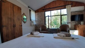 A bedroom with a large bed, two armchairs, a stone wall, a wooden ceiling, and a television. - Butik Hotel Masukiye (Kartepe)
