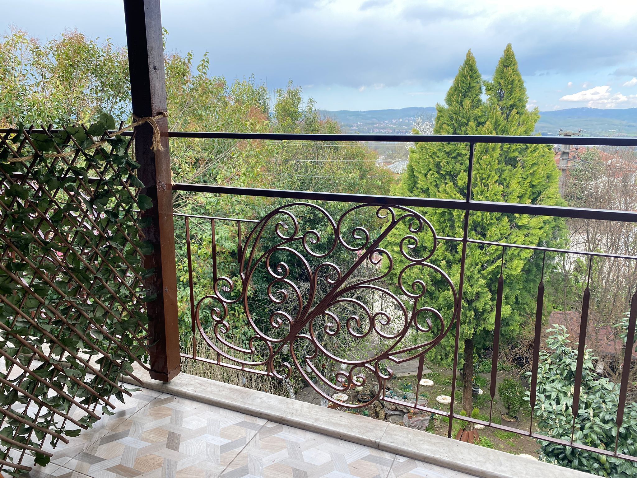 A balcony with a wrought iron railing overlooking a garden and distant landscape.