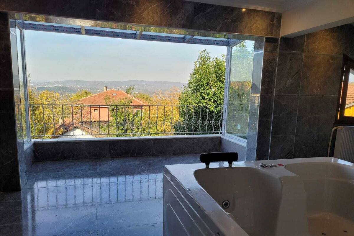 A modern bathroom with a large bathtub, a view of a cityscape, and a balcony with a metal railing.