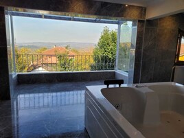 A modern bathroom with a large bathtub, a view of a cityscape, and a balcony with a metal railing.
