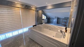 Un baño moderno con una bañera grande, suelo de mármol y una ventana con persianas.