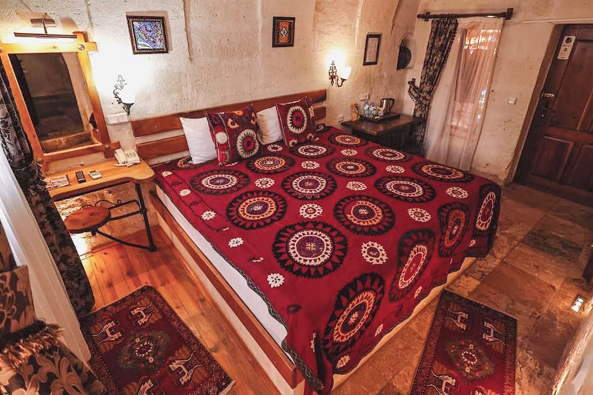 A bedroom with a large bed, a wooden desk, a mirror, and a nightstand.